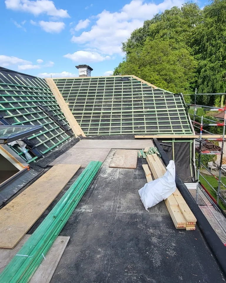 Deux pans de toiture lattés au-dessus d’une partie plate, bottes de lattes et panneaux sur le chantier