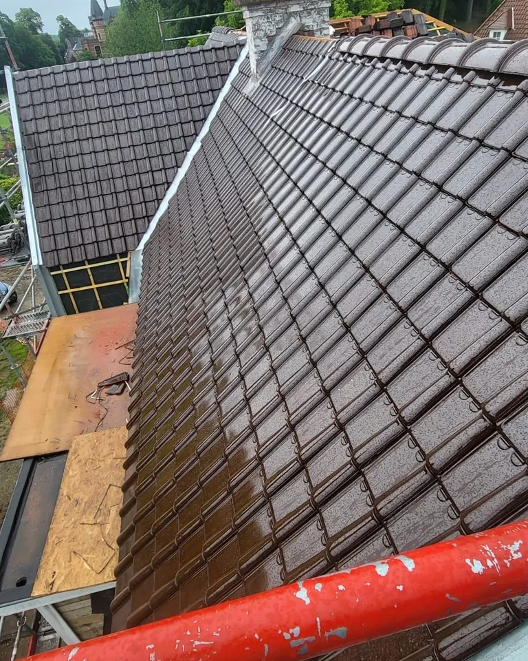 Tuiles brun foncé posées sur un pan, mouillées par la pluie, raccord en zinc le long de la cheminée, échafaudage au premier plan