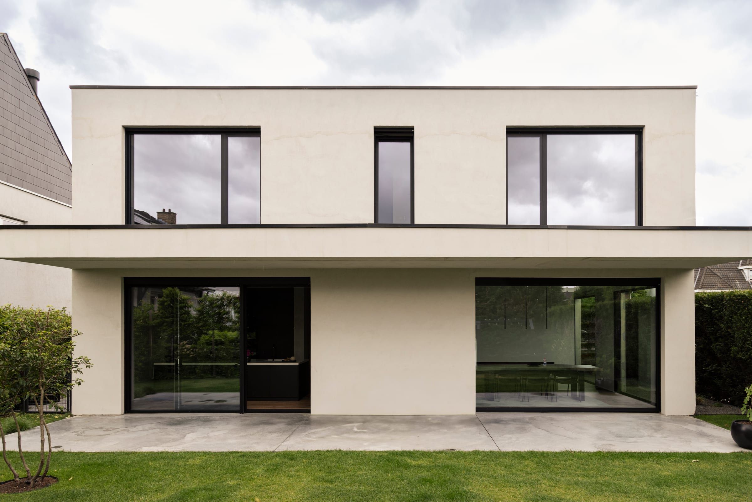 La même façade après la livraison, photographiée en mai 2025 : enduit clair, baies vitrées noires, terrasse en béton et pelouse