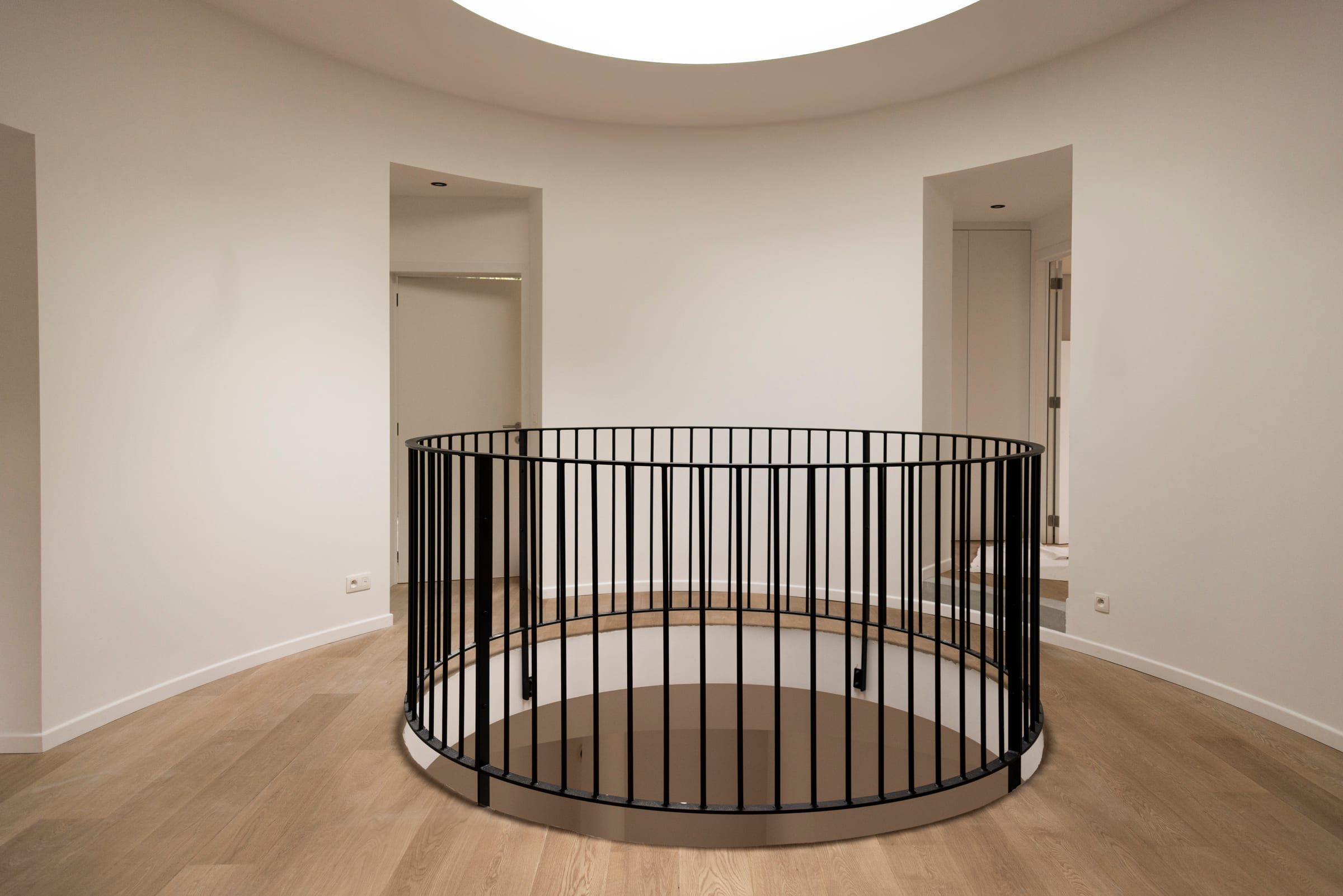 Salon circulaire rénové, colonnes blanches, garde-corps en fer forgé autour de l’ouverture de l’escalier et parquet en chêne
