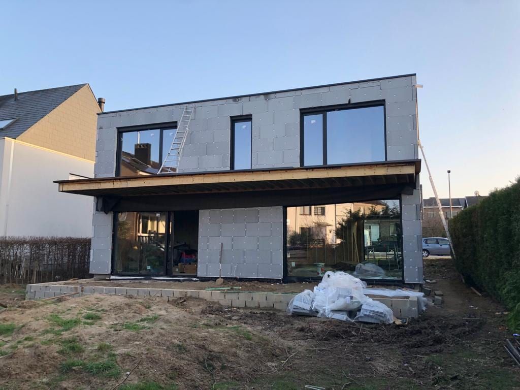Façade arrière de la villa pendant le chantier : blocs isolants apparents, châssis posés, terrasse en travaux