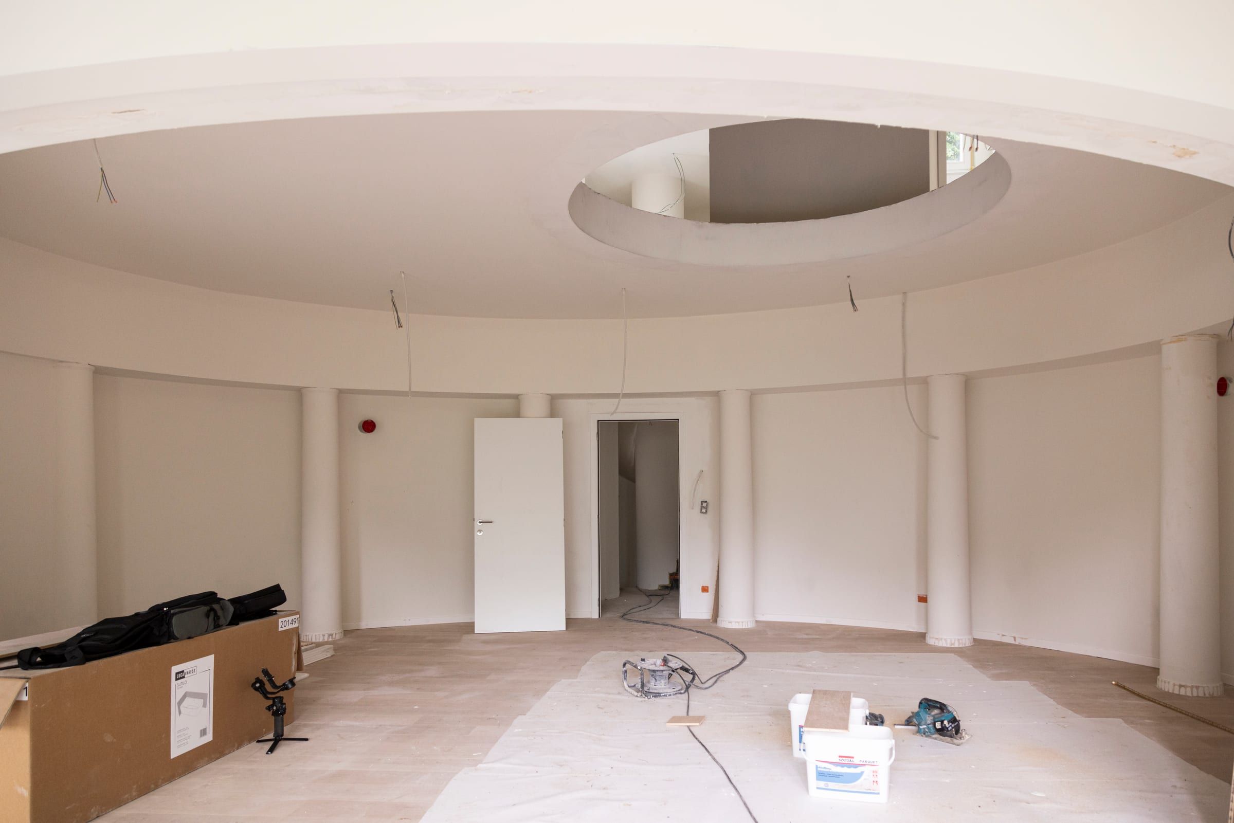 Salon circulaire pendant le chantier : colonnes et plafond enduits, câbles en attente, ouverture ronde vers l’étage, sol protégé