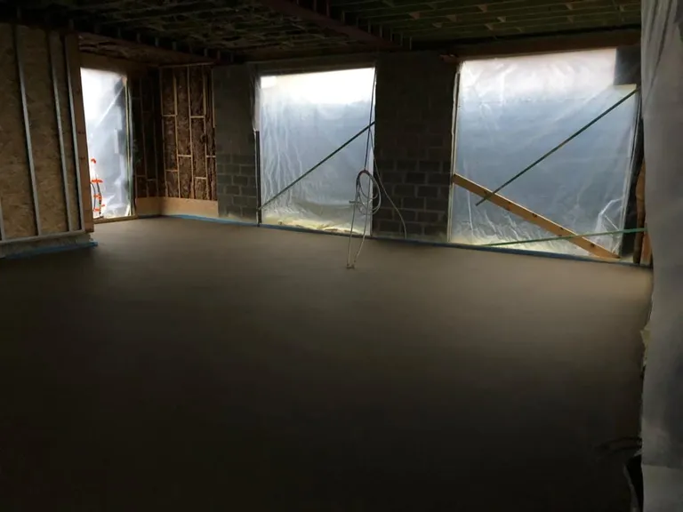 Chape fraîchement coulée dans une pièce en chantier, baies protégées par des bâches