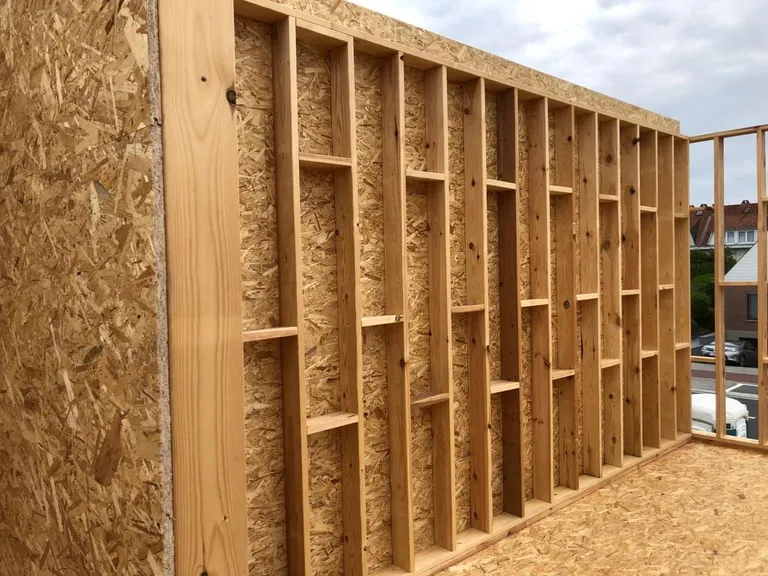Mur en ossature bois : montants de l’ossature devant un panneau, maisons voisines en arrière-plan