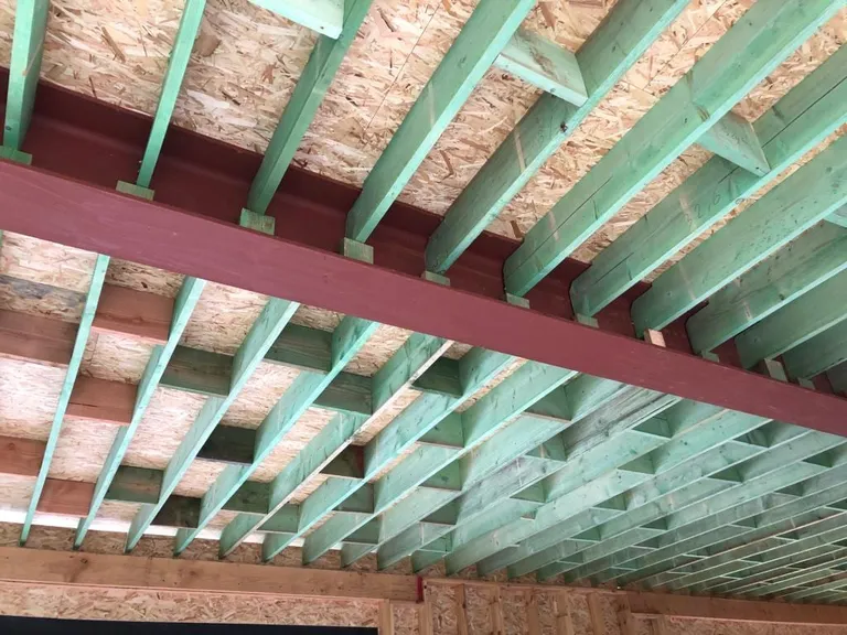 Poutres en bois traité reposant sur une poutre en acier peinte, panneaux de plancher au-dessus