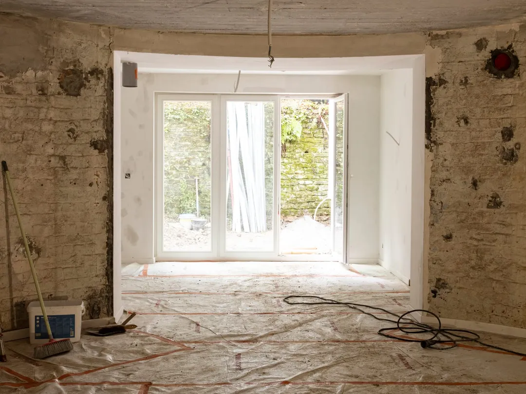 Pièce mise à nu dans une maison en rénovation : murs en brique, plafond en béton, nouvelle baie ouverte sur le jardin
