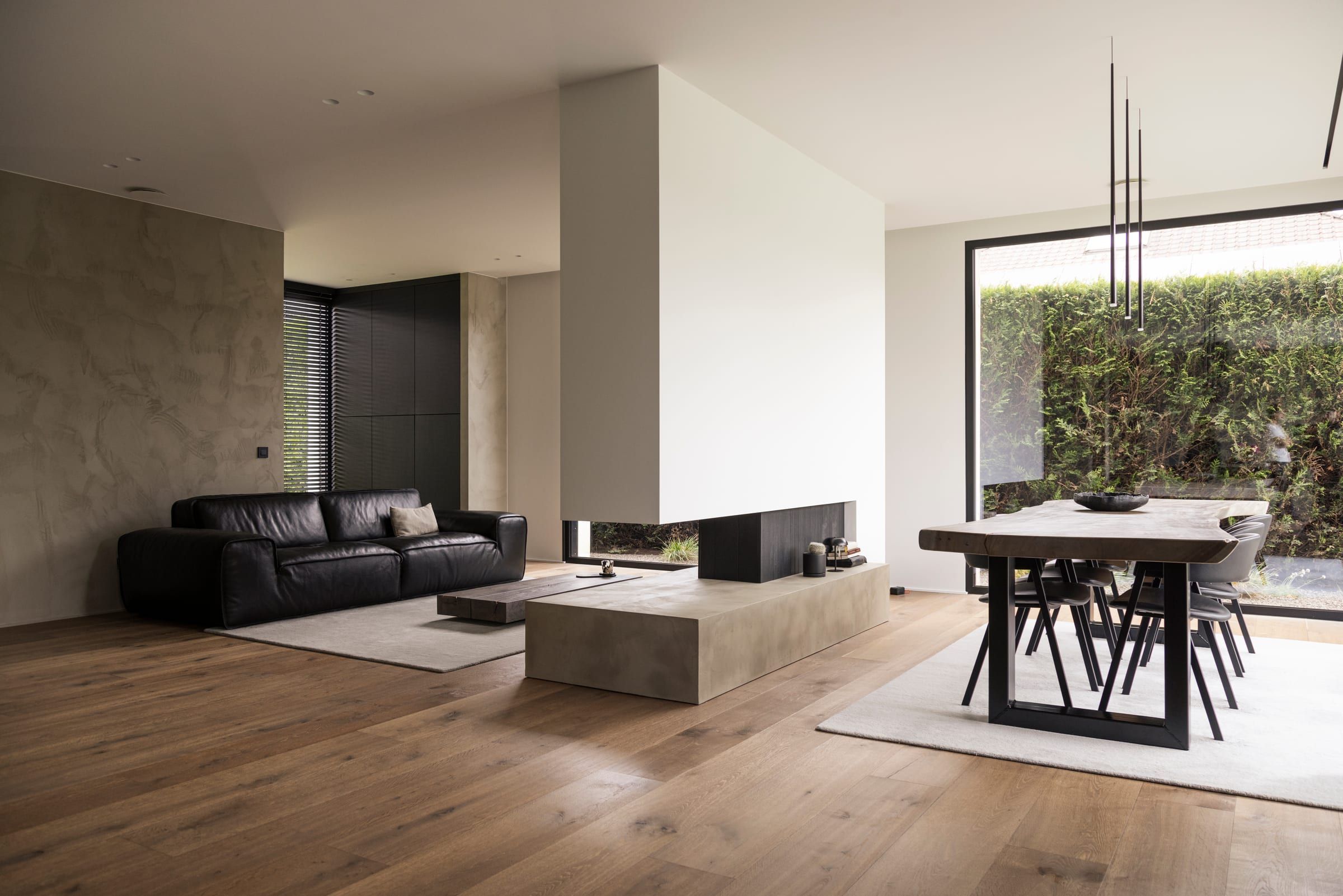 Séjour et salle à manger d’une villa contemporaine, murs en béton ciré, parquet en chêne et grandes baies vitrées sur le jardin