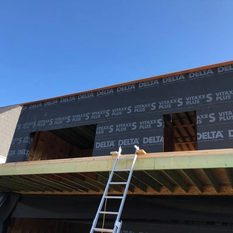 Étage en ossature bois d’une villa en chantier, membrane de protection posée, poutres de la toiture plate et échelle